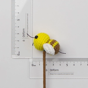 Detailed view of a handmade crochet bee decoration with dimensions shown on rulers
