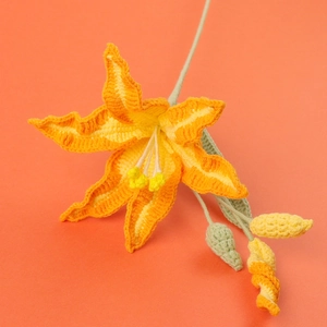 Close-up of handmade crochet lily flower with orange gradient petals and green leaves
