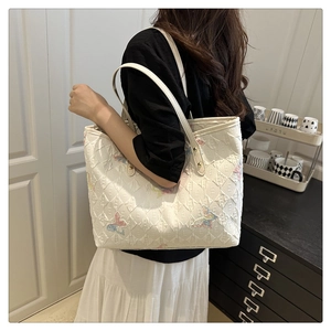 Detail of quilted canvas tote bag featuring colorful butterfly embroidery and shoulder strap