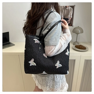 Close-up of black quilted canvas tote bag featuring colorful butterfly embroidery details