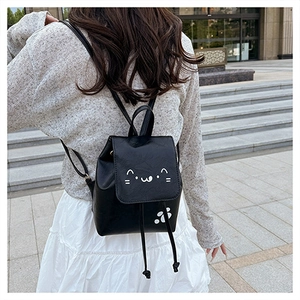 Outdoor shot of a black PU leather mini backpack featuring a cute white cartoon cat face