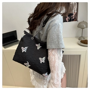 Detail of black pleated tote bag with colorful butterfly embroidery and chain strap