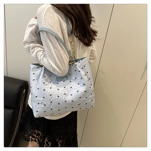 Detail of light blue quilted tote bag with black bows and gold chain shoulder strap