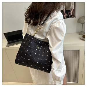 Detail of black quilted tote bag with white bow patterns and gold chain handles