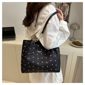 Détail du sac bandoulière noir matelassé avec motifs nœuds blancs et chaîne dorée