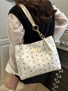 White quilted tote bag with black bow embroidery and gold ring strap displayed on shoulder