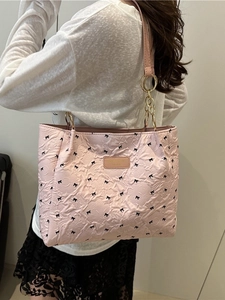 Pink pleated tote bag with black bow patterns and gold chain link worn by model