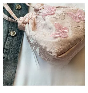 Close-up of pink bucket bag featuring 3D butterfly embroidery and pearl drawstring detail