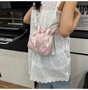 Detail of pink embroidered butterfly pattern and white pearl drawstring on bucket bag