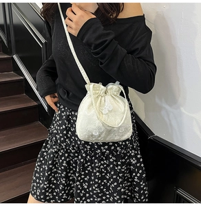 Detailed view of floral butterfly embroidery on white lace drawstring bucket bag