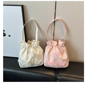 Detail showing delicate butterfly embroidery on satin drawstring bucket bags in cream and pink