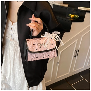 Close-up of pink handbag featuring pleated texture, metal bow, and pearl charm detail