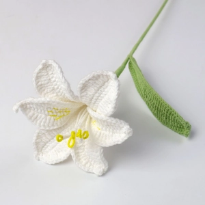 Handmade crochet white lily flower with yellow stamen and green leaves on white background