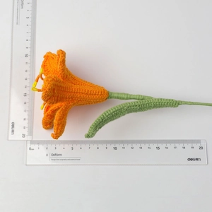 Macro view of handmade crochet lily flower with orange petals and detailed green stem