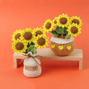 Two handmade crochet sunflower potted plants on a wooden stool with a bright orange background