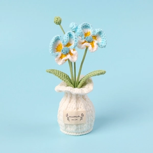 Handmade crochet pansy flower pot with blue and white petals in a small woven vase