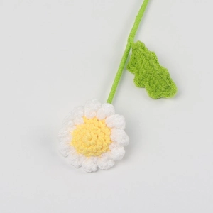 Close-up of handmade crochet daisy flower with yellow core and green knitted leaf