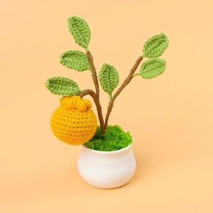 Detailed close-up of a handmade crochet orange plant with green leaves in a white ceramic pot