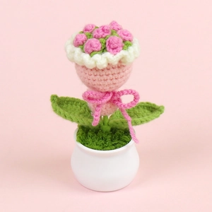 Detailed close-up of handmade crochet pink rose in white pot with green leaves