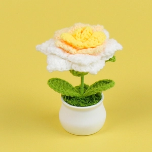 Macro shot of handmade crochet rose plant with white and orange petals in a white pot