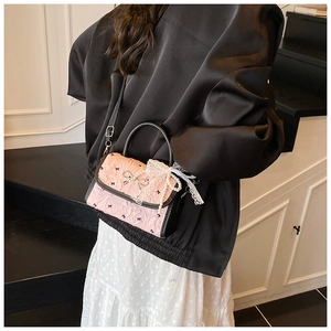 Detailed view of pink pleated handbag with black bows and pearl charm on a model