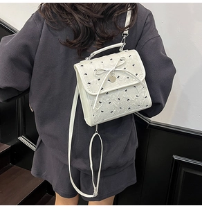 Dettaglio di una borsa bianca con fiocchi neri e ciondolo a cuore indossata dal modello