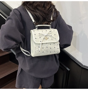 Dettaglio dello zaino in seersucker bianco con fiocchi neri e ciondolo a cuore