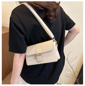 Detail shot of beige crocodile embossed crossbody bag with gold buckle on shoulder