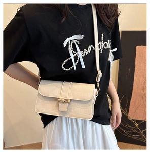 Detail of a white crocodile embossed shoulder bag with a gold bamboo clasp on a model