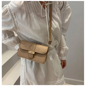 Detail of beige crocodile pattern handbag with gold clasp and leather shoulder strap