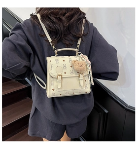 Close-up of cream backpack featuring teddy bear prints and plush charm on the strap