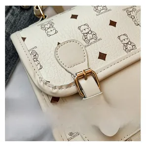 Close-up of litchi grain leather texture and cartoon bear pattern on beige shoulder bag