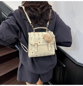 Detail of a beige mini bear backpack featuring a plush charm and decorative scarf