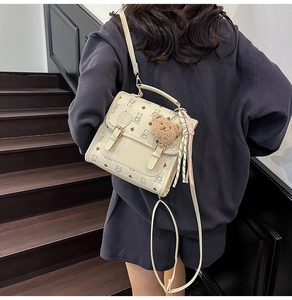 Detail of cream backpack with bear prints and decorative plush pendant on stairs