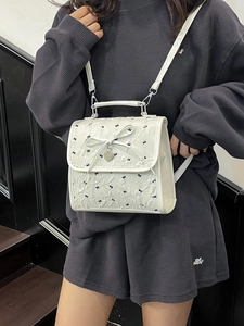 Borsa a spalla chic bianca testurizzata con fiocchi neri e ciondolo a cuore su modella