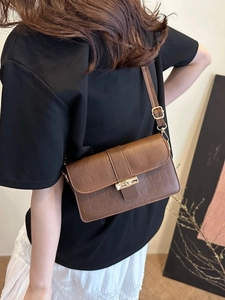 Brown crocodile-pattern underarm bag with gold bamboo clasp shown on shoulder
