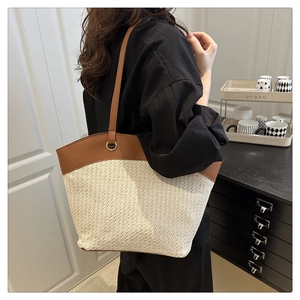 Detail of the woven straw tote bag featuring brown faux leather straps and metal rings