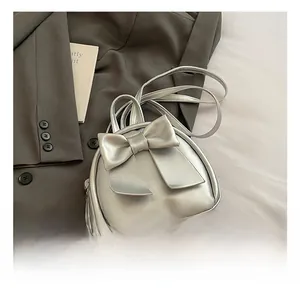 Close-up of a silver leather backpack featuring a large decorative bow and slim straps