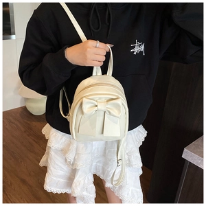 Detail of cream faux leather mini backpack featuring a decorative oversized bow and zipper