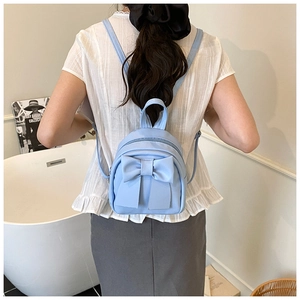 Back view of model wearing a mini light blue backpack with a large decorative bow detail