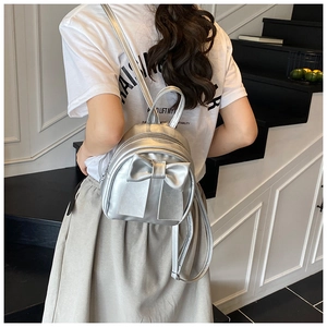 Silver metallic mini backpack with bow detail shown on model in a minimalist setting