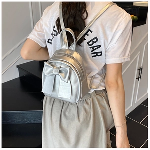 Close-up of a silver mini backpack with a decorative bow on a model against stairs