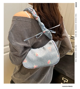 Detail of pink rose embroidery and bow strap on light blue denim underarm shoulder bag