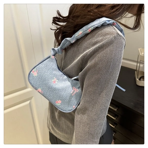 Detail of light blue denim shoulder bag with pink roses, bows and ruffled strap detail