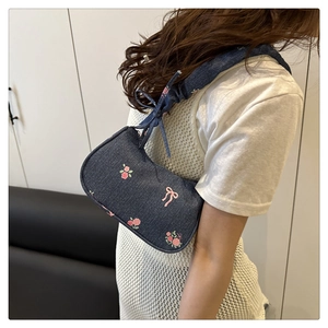Detail of blue denim shoulder bag featuring pink rose patterns and pleated strap