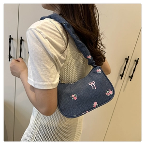 Detail of navy denim shoulder bag featuring pink embroidered rose and bow on shoulder