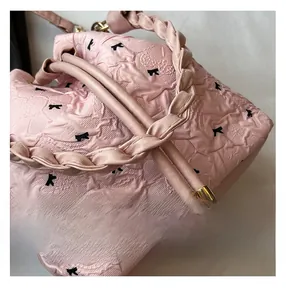 Nahaufnahme der rosa Plissee-Schultertasche mit schwarzen Schleifen und Webgriff
