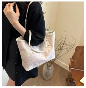 Detail of a pink floral tote bag with white leather straps in a cozy indoor setting