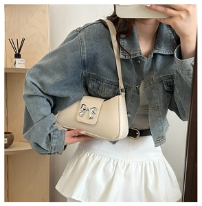 Sac sous le bras blanc crème avec boucle noeud argenté porté avec une tenue en jean