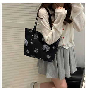 Détail du sac cabas noir à motifs floraux blancs et rivets dorés sur la bandoulière